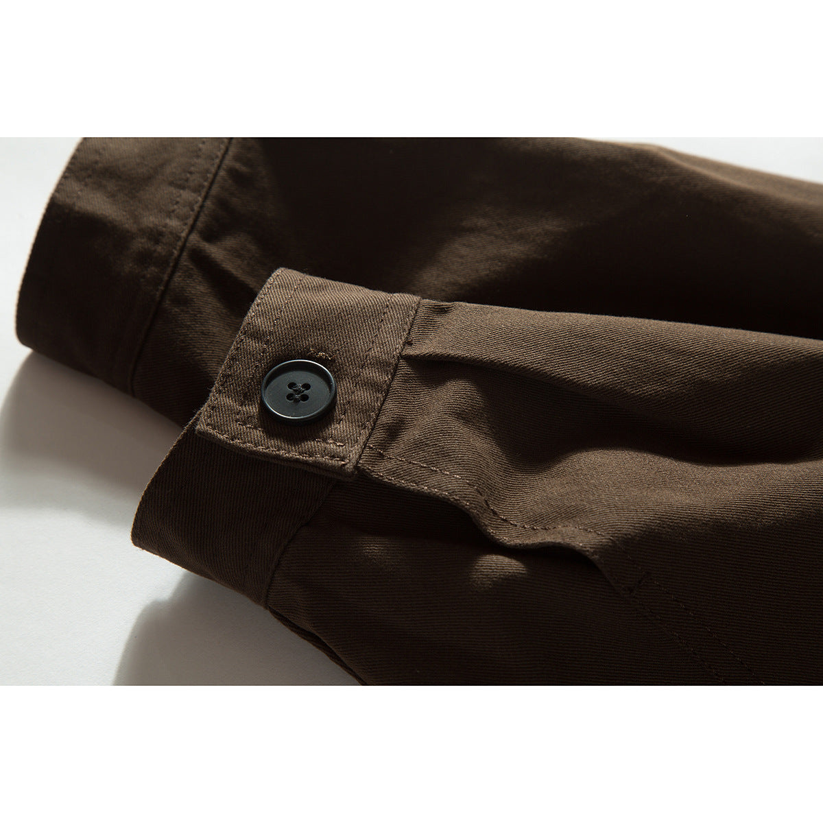 Close-up of a dark brown shirt cuff with a black button and stitched button tab.