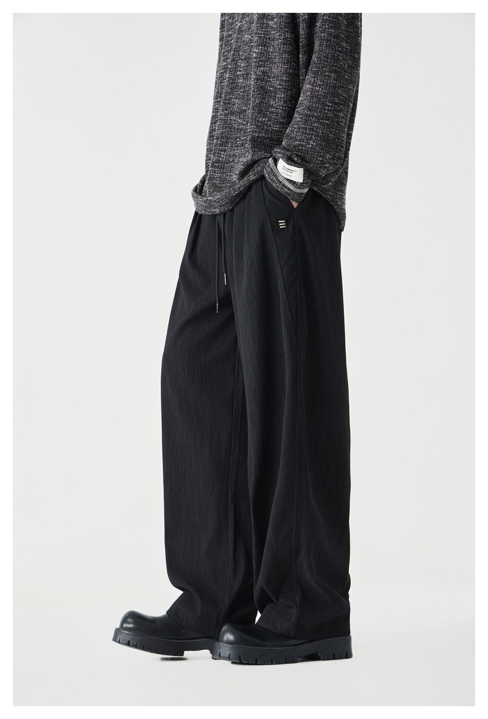 Side view of model in black wide-leg pleated drawstring pants, gray knit sweater and chunky black boots