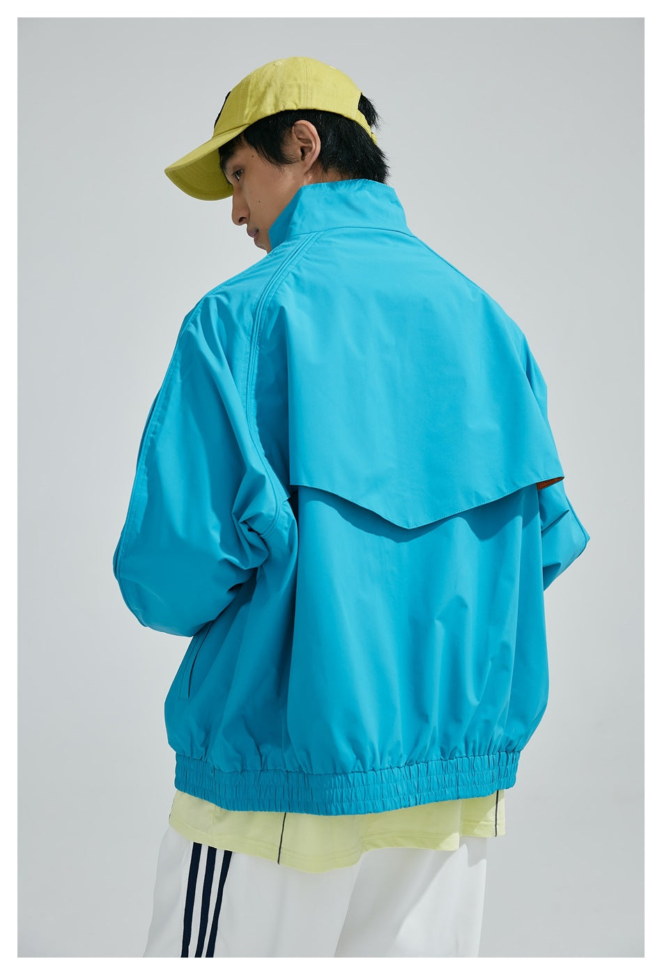 Model wearing a bright turquoise jacket with a high collar and back vent, viewed from behind.