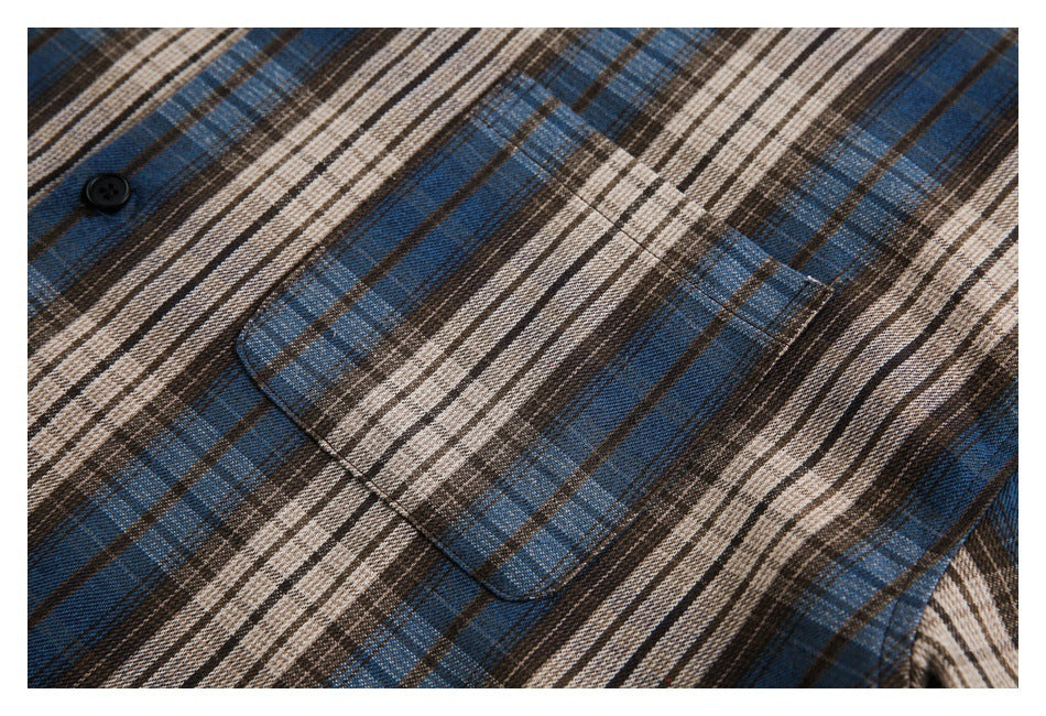 Close-up of a blue, brown, and cream plaid shirt showing a black button and chest pocket.