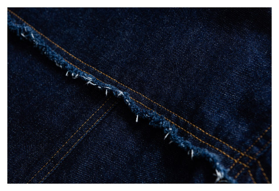 Close-up of a frayed denim seam with orange stitching against dark indigo fabric.