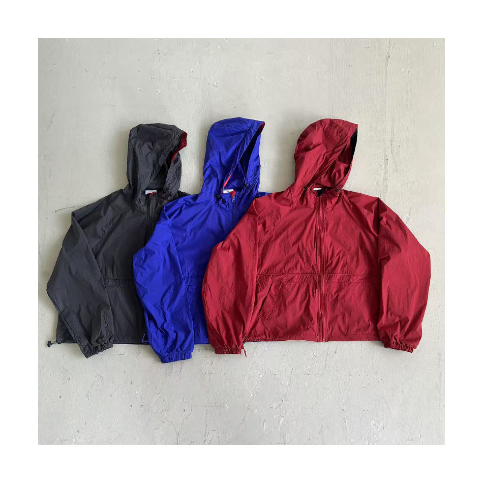Black-gray, blue and red hooded zip jackets laid flat side by side on a concrete floor