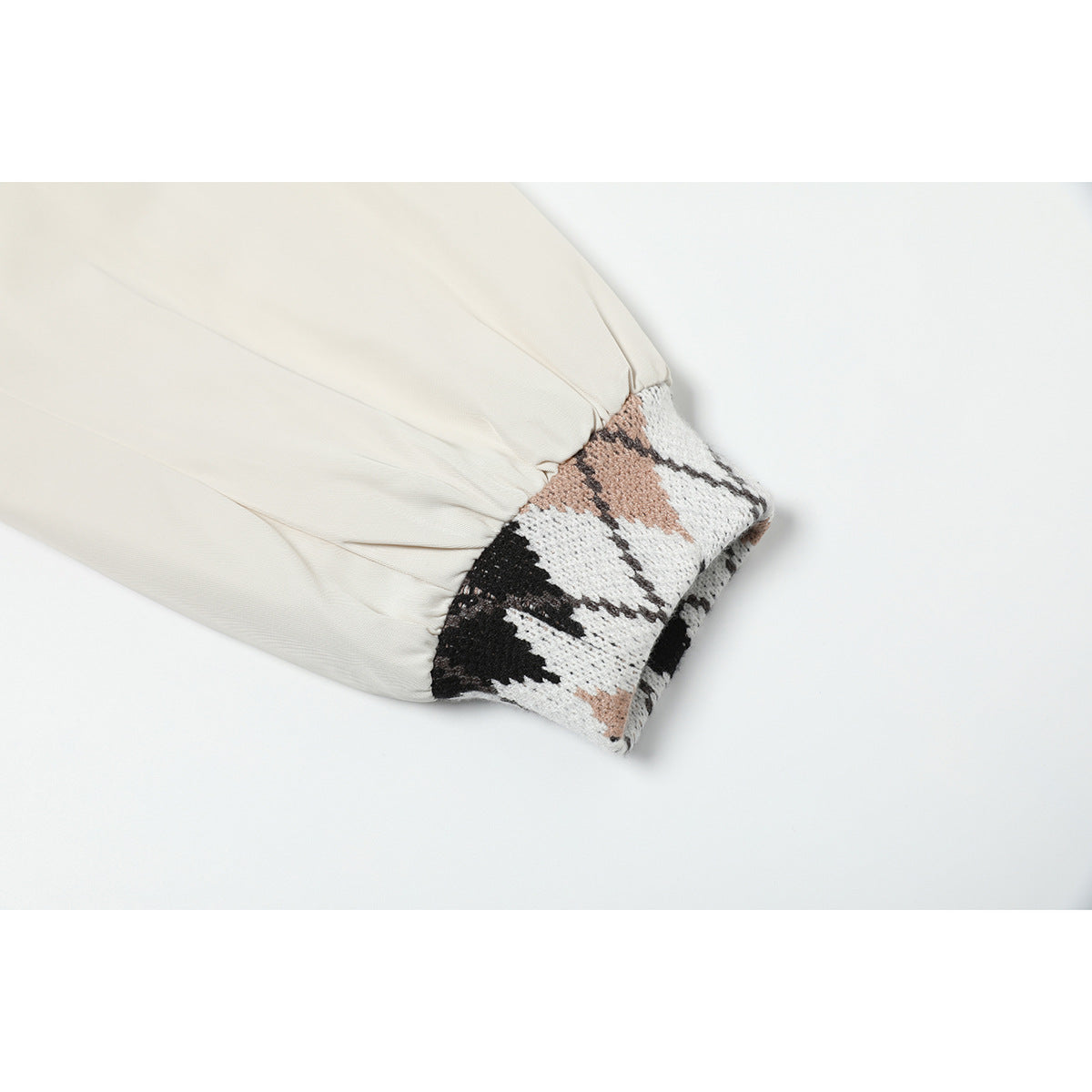 Close-up of an ivory jacket sleeve gathered into a black, white, and tan diamond-pattern knit cuff.