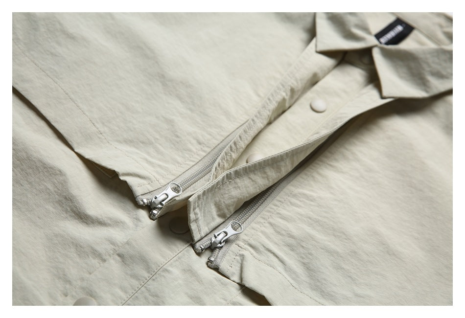 Close-up of a light beige shirt jacket showing two silver zippers and a snap-button placket.