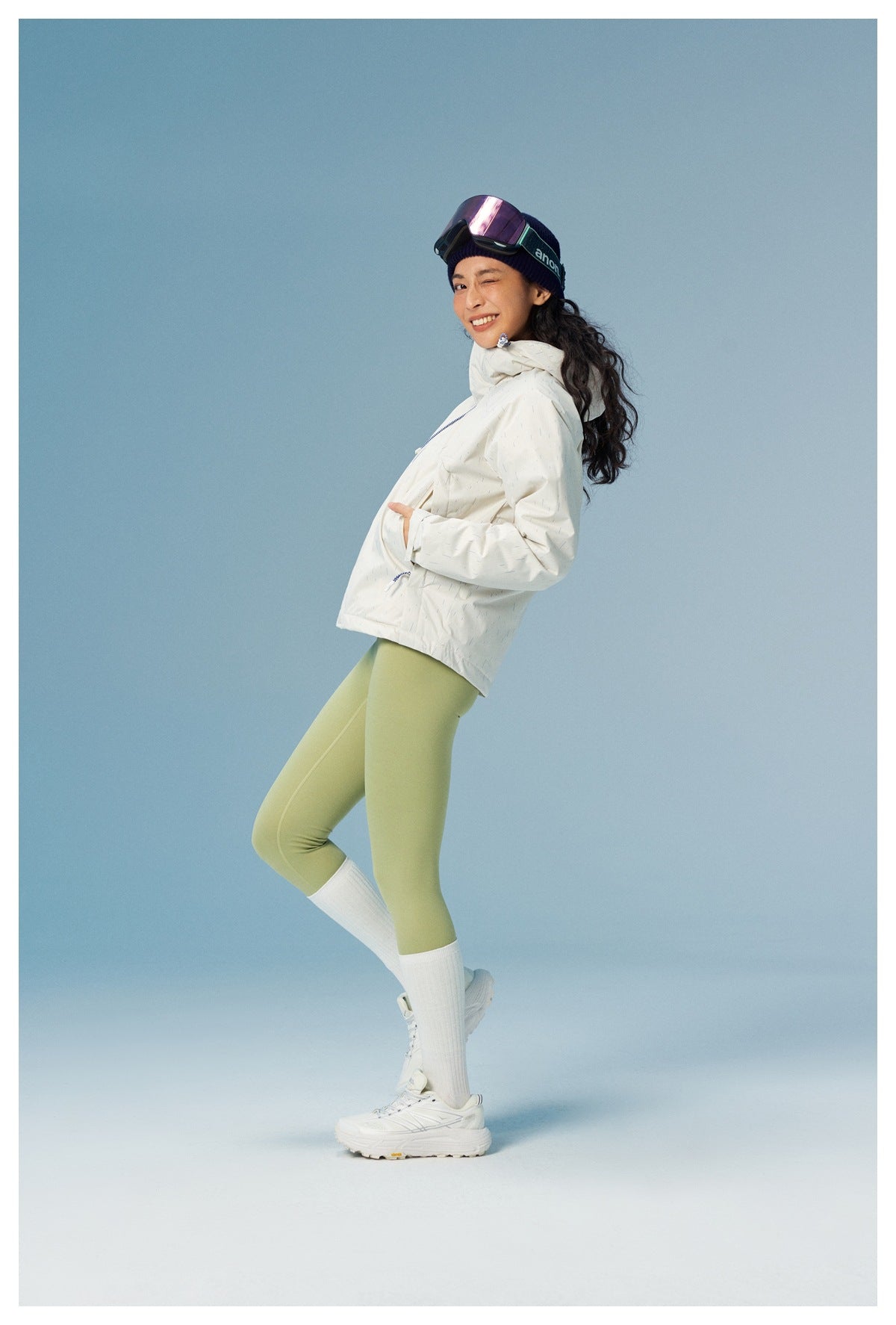 Model in a white patterned hooded jacket and pale green leggings, posing at an angle with hands in the pockets.