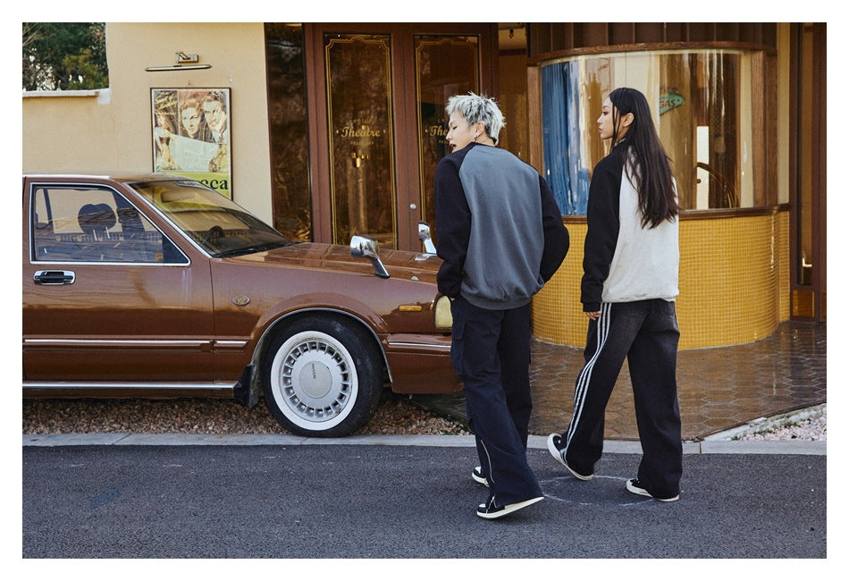 Two models walk away, showing the backs of charcoal-and-black and white-and-black raglan sweatshirts.