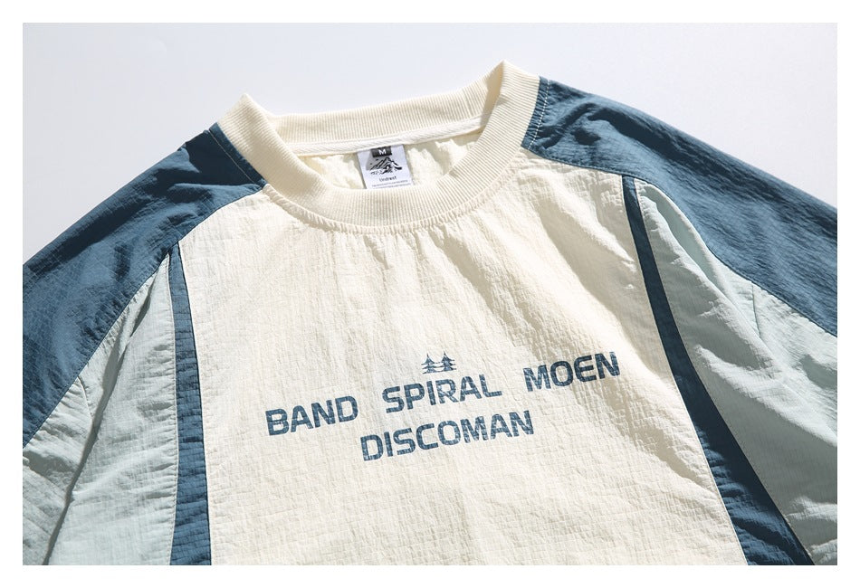 Close-up of the shirt's cream front, blue and pale sage shoulder panels, ribbed collar, and dark blue printed lettering.