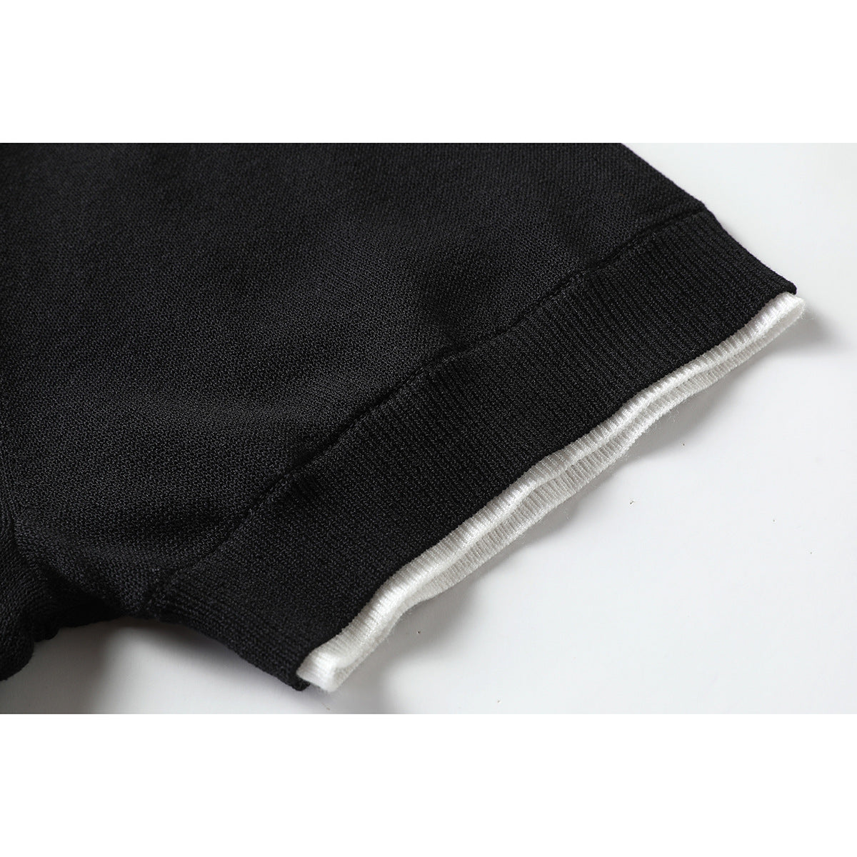 Close-up of a black knit sleeve hem layered over a narrow white ribbed edge.