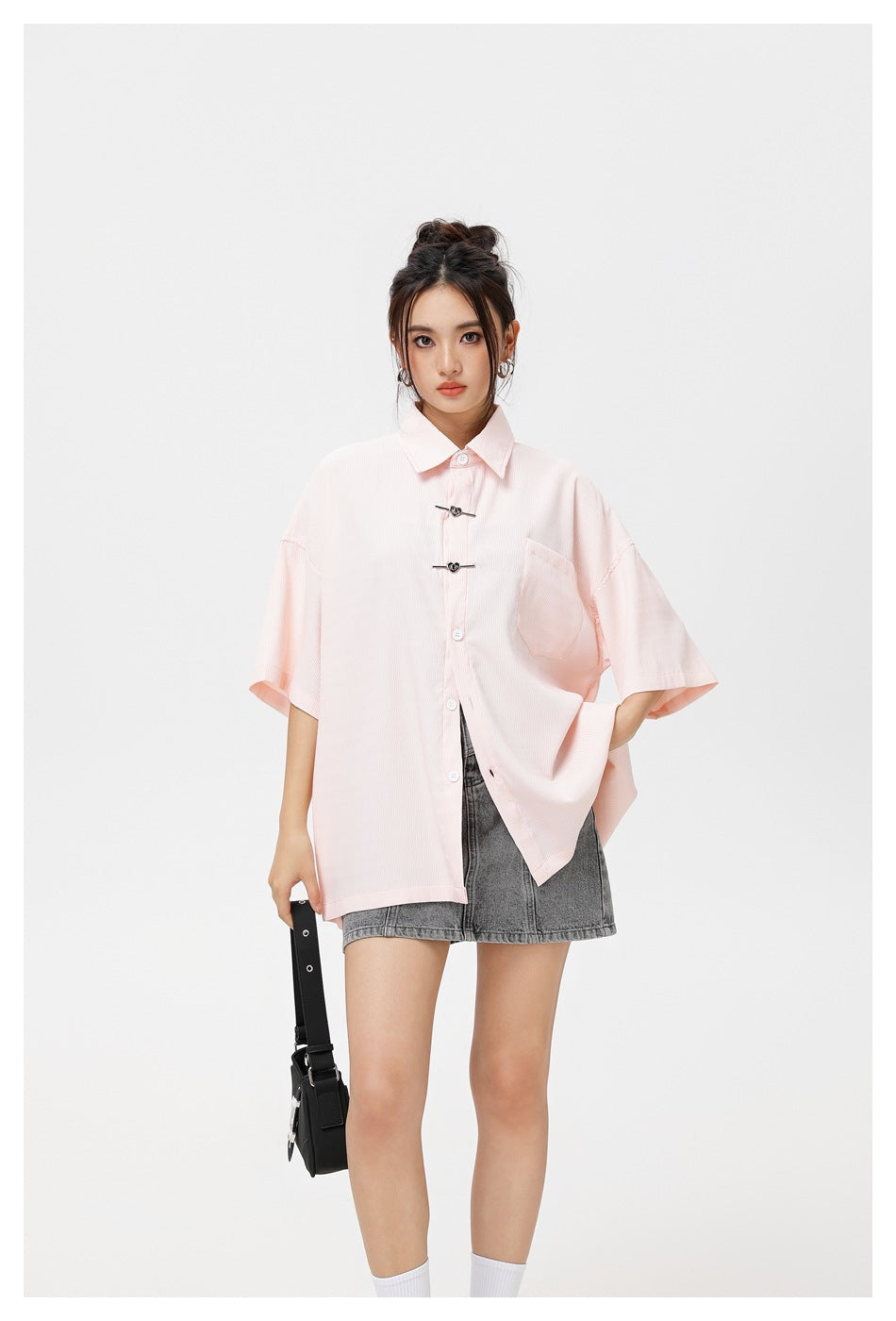 Closer view of a model wearing a pale pink oversized short-sleeve shirt with a chest pocket and decorative front clasps.
