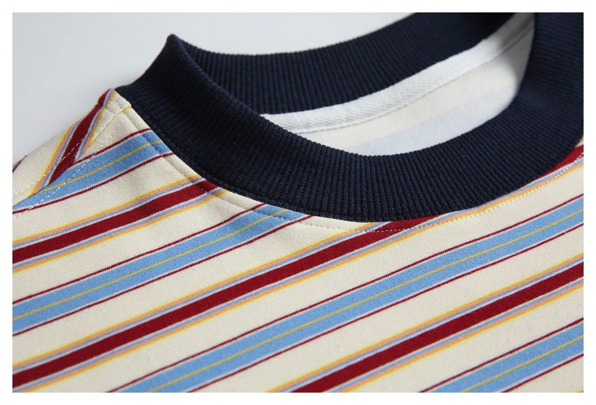 Close-up of a cream T-shirt with narrow blue, burgundy and yellow stripes and a dark ribbed crew neckline.
