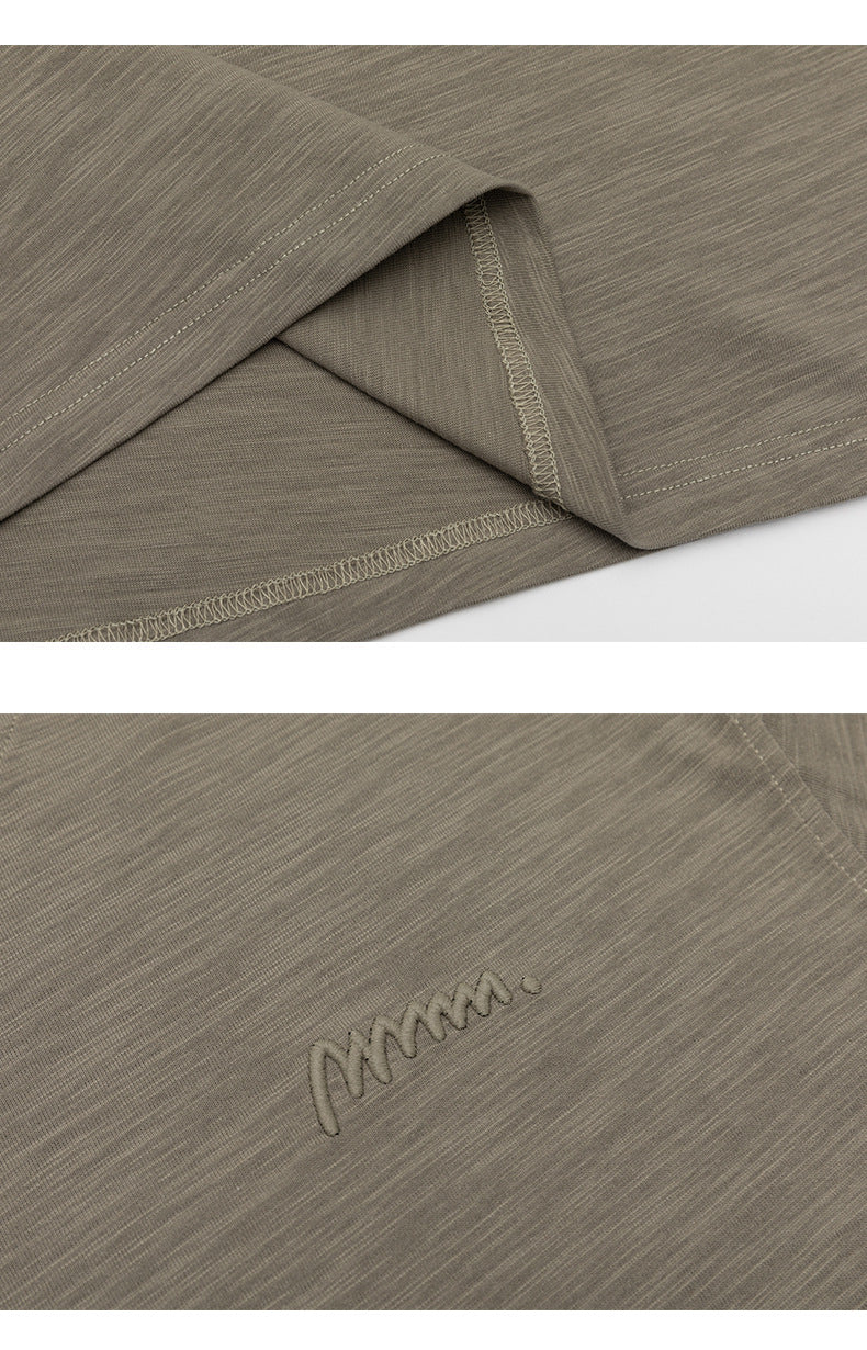 Close-up details of a taupe T-shirt’s stitched hem and small embroidered chest logo.