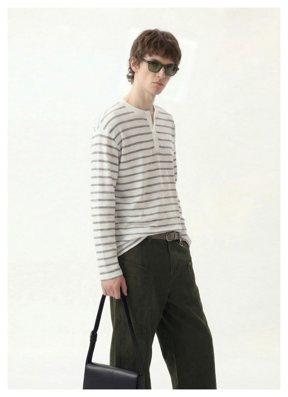 Three-quarter view of a model wearing a white and gray striped henley and dark olive pants.