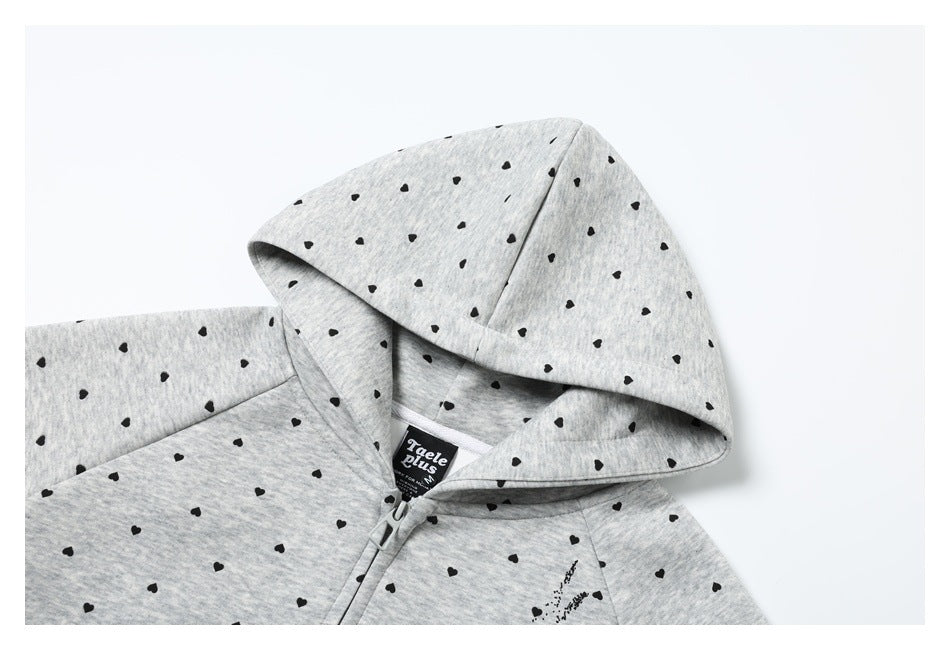 Close-up of a light gray zip-up hoodie with black heart prints, showing its hood and zipper.