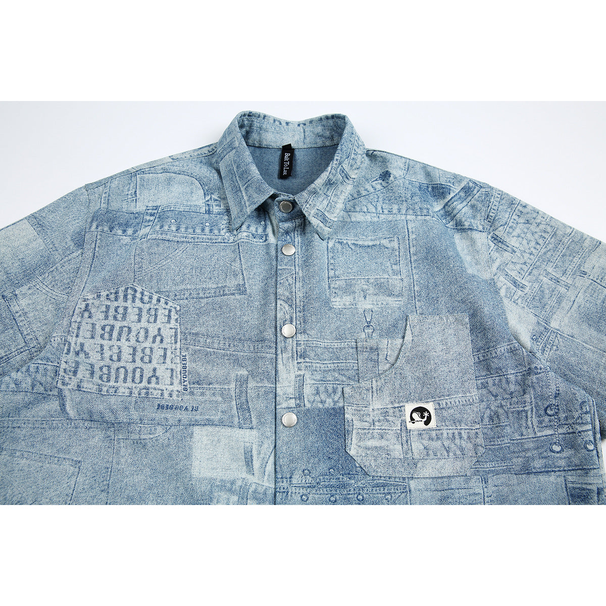 Close view of a light blue patchwork-print denim button-up shirt with pointed collar, chest pockets and metal snaps.