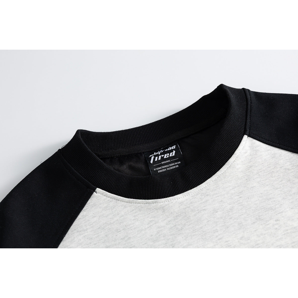 Close-up of a black ribbed crew neck and shoulder panels on a light gray raglan shirt.