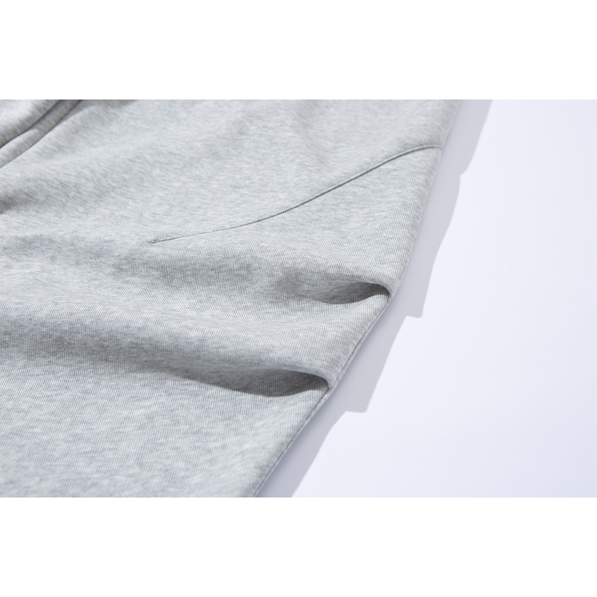 Close-up of light gray heather sweatpants showing a curved side seam and pocket opening.