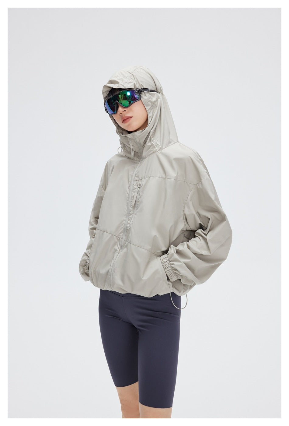 Model wearing a light gray hooded jacket with a chest zip pocket and dark navy cycling shorts.