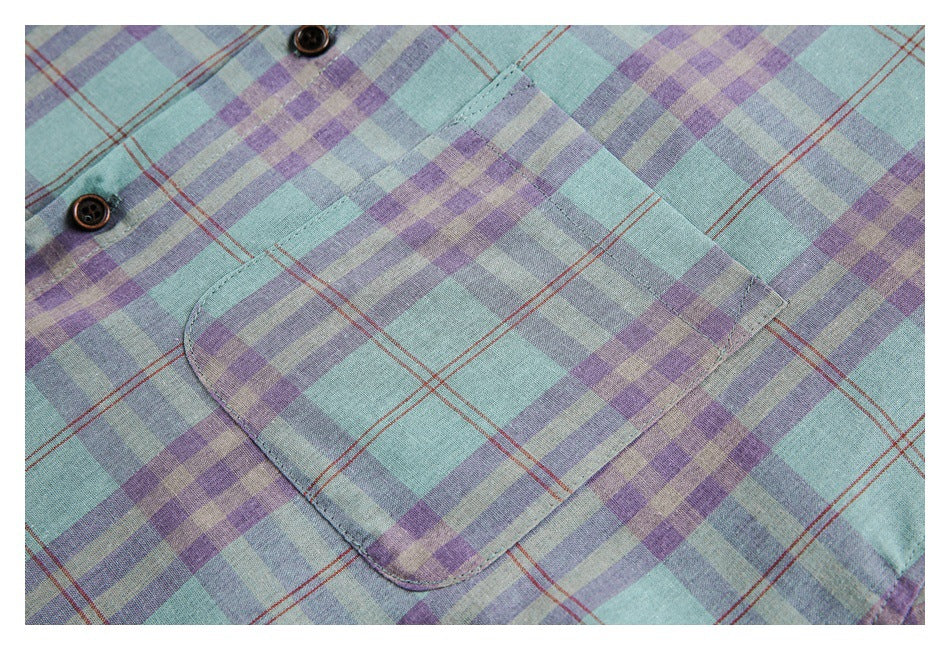 Close-up of a chest pocket and dark buttons on a mint, lavender, and gray plaid shirt with thin rust-red lines.