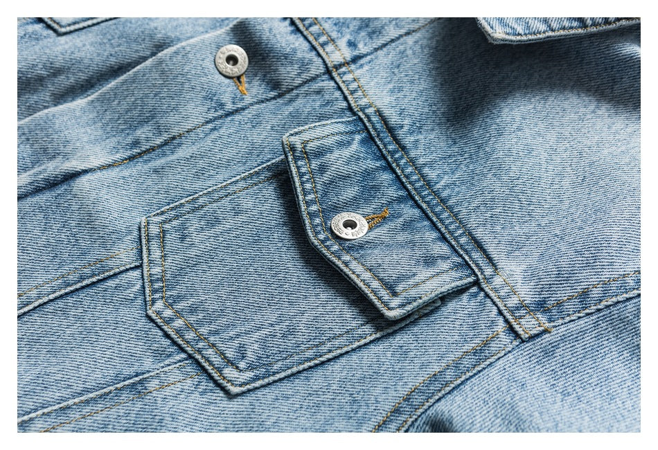 Close-up of a light blue denim jacket pocket flap, metal buttons, and contrast stitching.