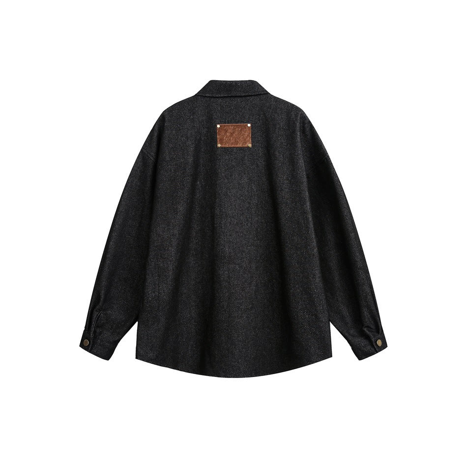 Back view of a black long-sleeve collared jacket with a small brown patch and buttoned cuffs, on white.