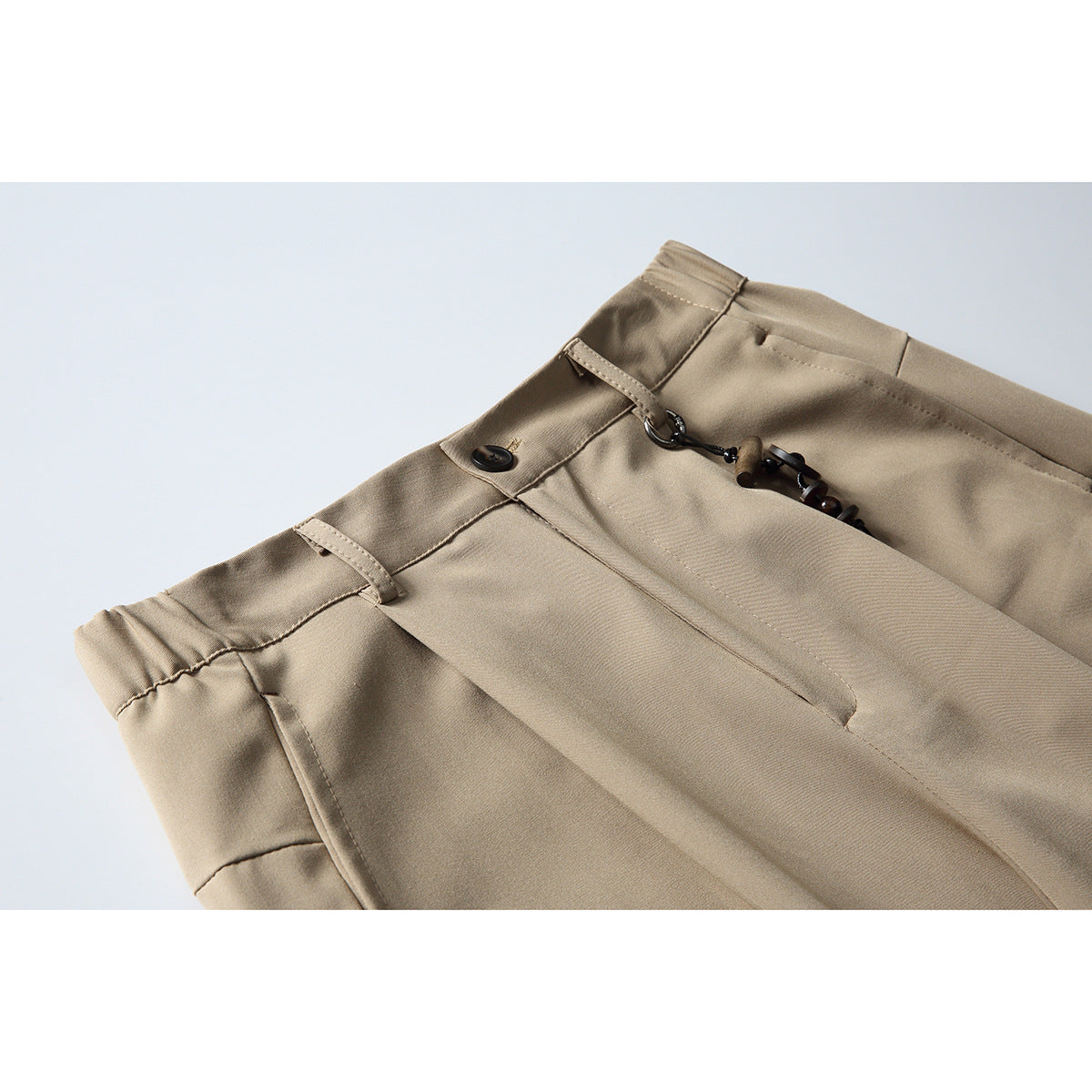 Close-up of beige trousers showing the waistband, belt loops, button, and decorative cord detail.