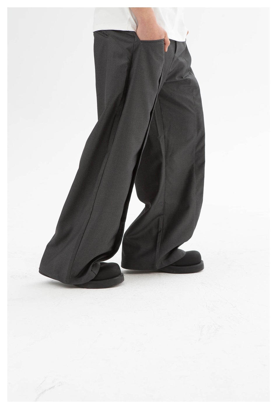 Model wearing charcoal gray wide-leg trousers with a white shirt and black shoes, shown from the waist down.