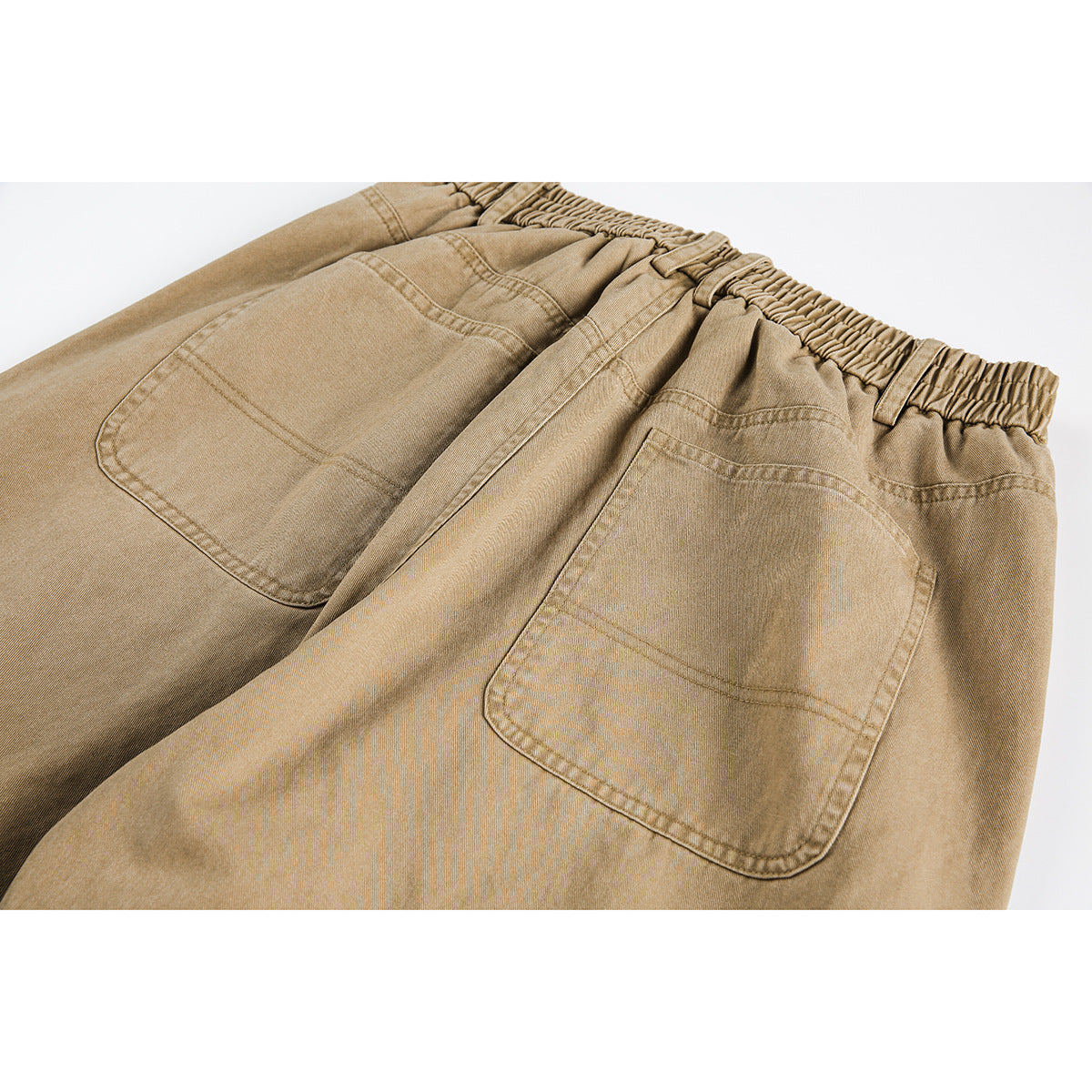 Close-up of tan trousers from the back, showing the elastic waistband and two patch pockets.