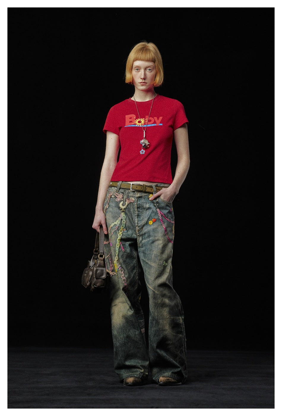 Model wearing the red cropped 'Baby' graphic T-shirt with distressed wide-leg jeans, standing against a dark background