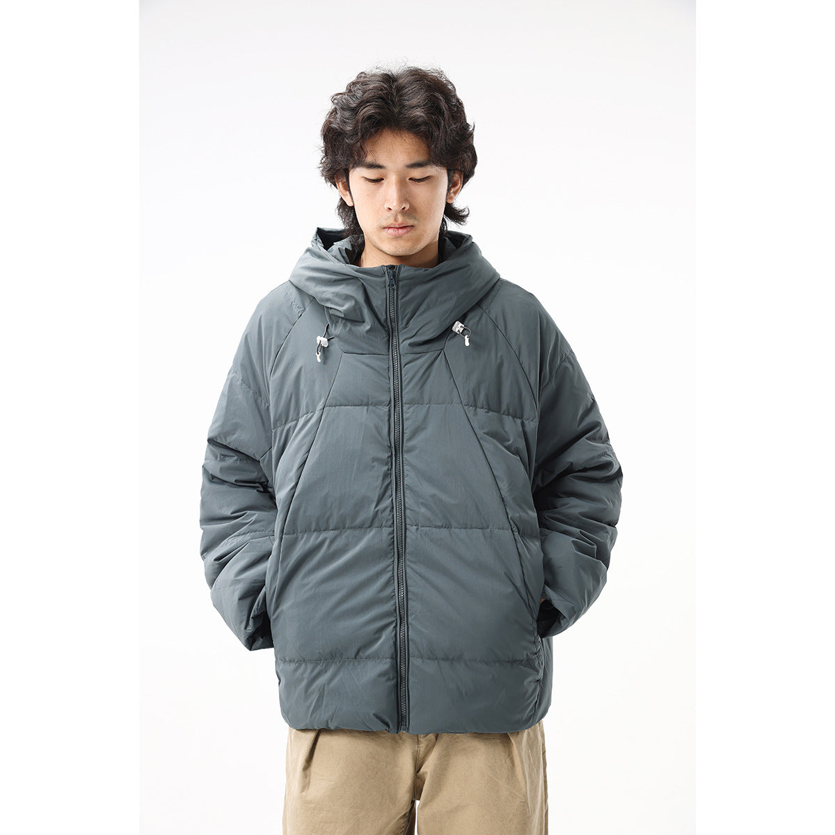 Front view of a model wearing a slate-gray hooded puffer jacket with a zip front and drawcord details.