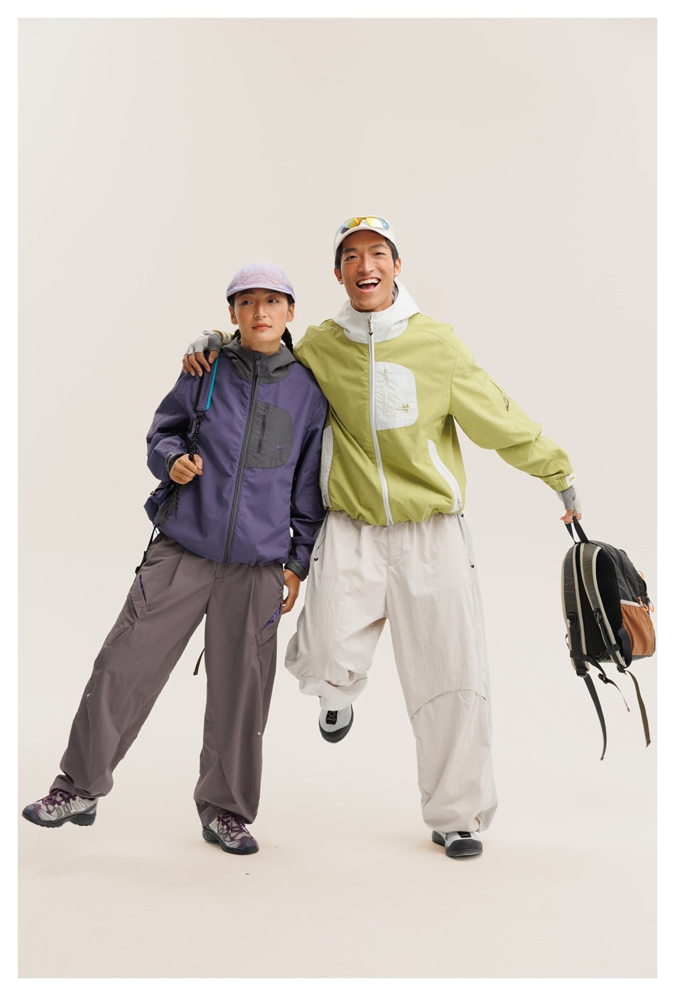 Two models pose in purple and charcoal, and lime-green and white outdoor jackets with loose trousers.