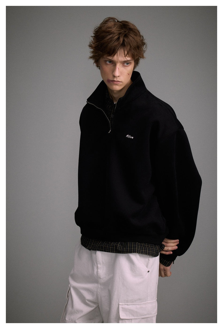 Model wearing a black quarter-zip sweatshirt with small white chest embroidery, shown with light cargo pants.