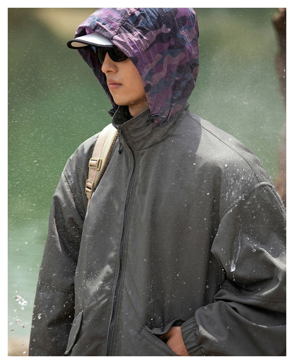 Person wearing the dark gray jacket with the purple camouflage hood up, with water droplets on the fabric