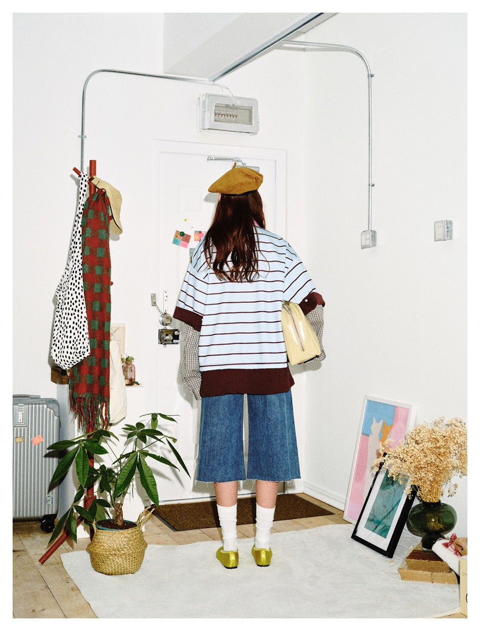 Back view of a model wearing an oversized light blue striped top with dark brown trim and layered checked sleeves.