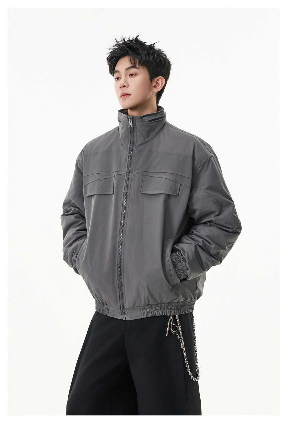 Three-quarter front view of a model wearing a gray zip jacket with a stand collar and flap chest pockets.