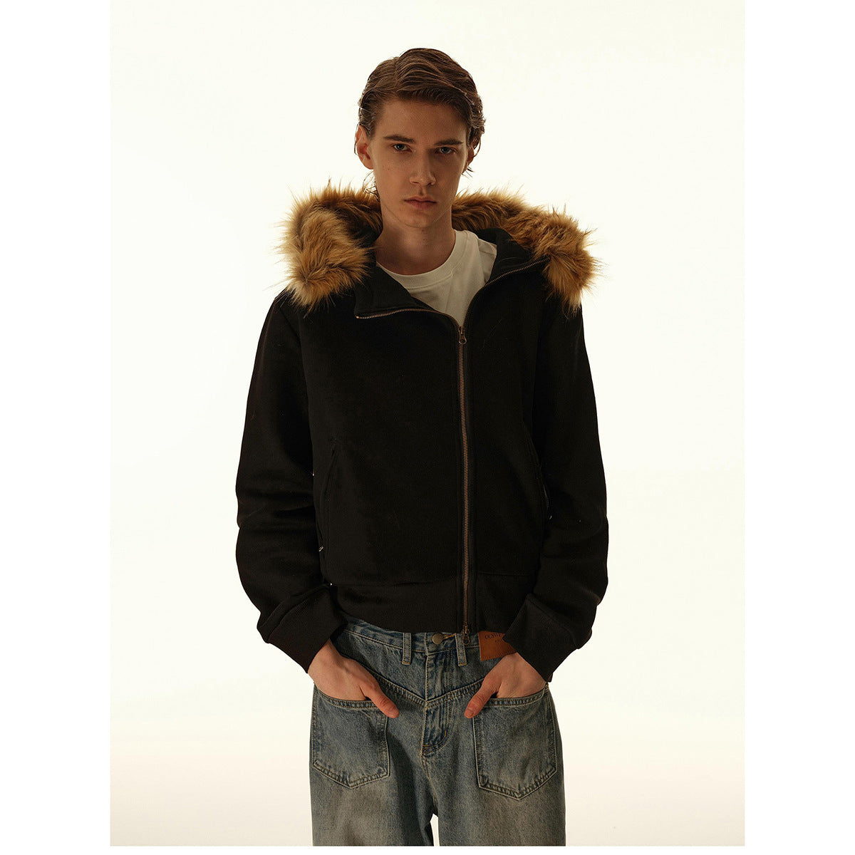 Man wearing a black zip-front hooded jacket with tan fur trim, ribbed cuffs and hem, and front pockets.