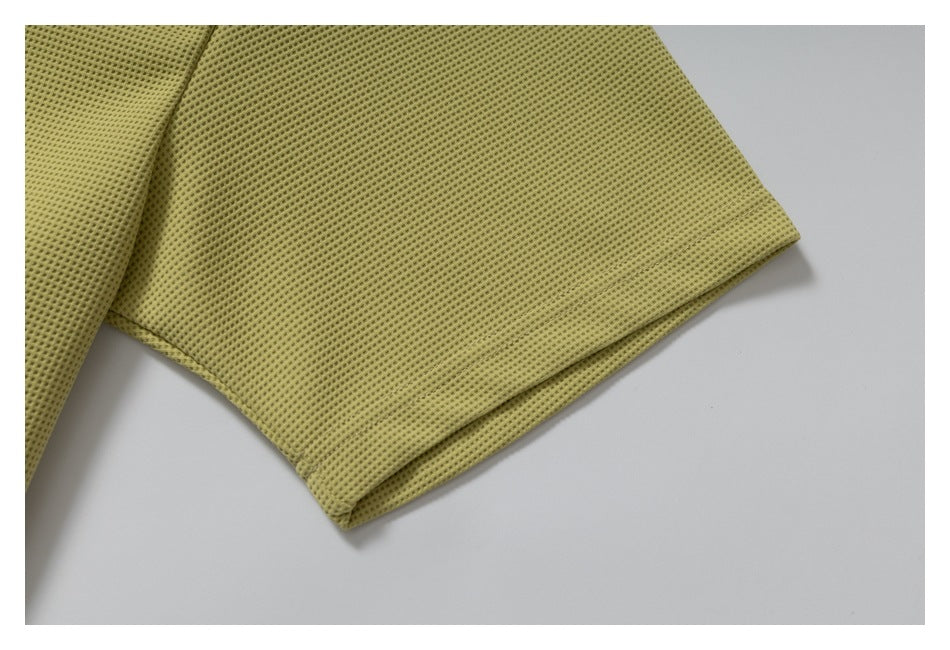 Close-up of a short sleeve and stitched hem on olive-yellow perforated knit fabric.