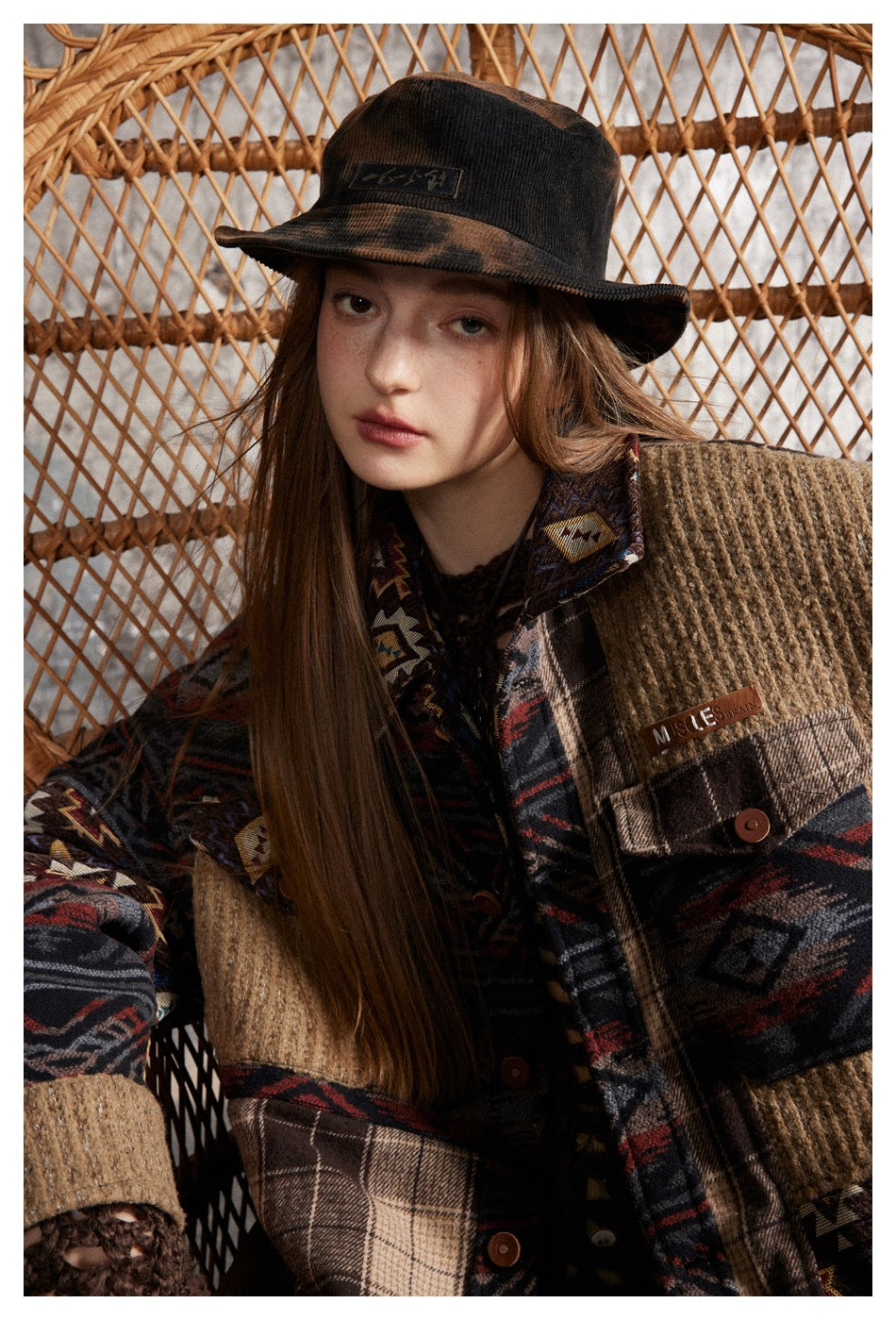 Close-up of a model wearing a patchwork jacket with patterned sleeves, tan textured panels, and a buttoned pocket.