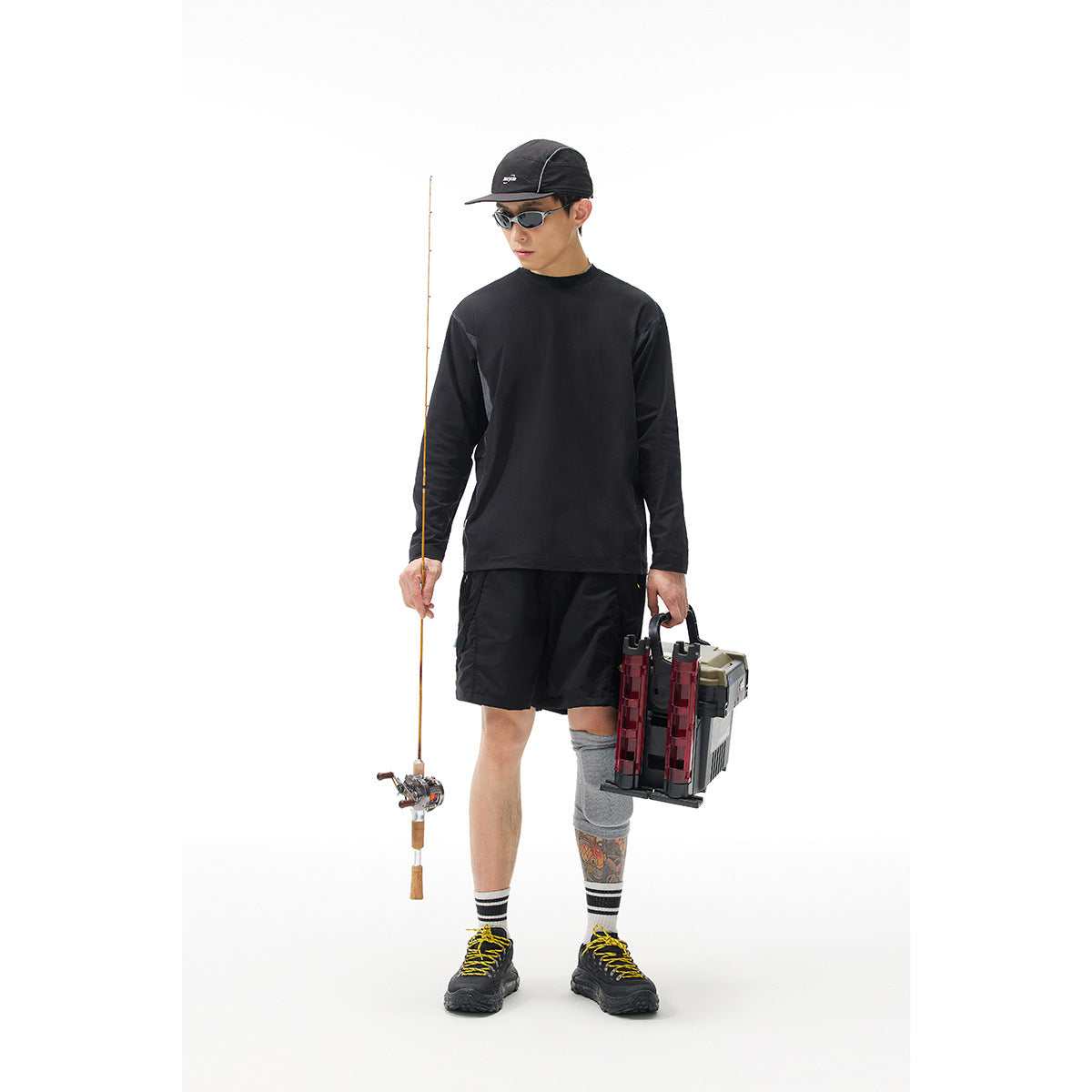 Front view of a model wearing a plain black long-sleeve shirt and black shorts with fishing gear.