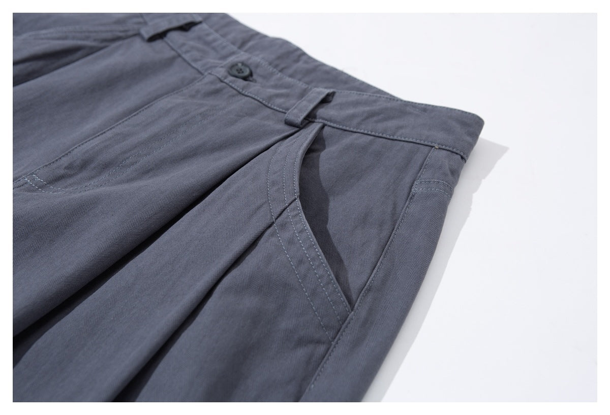 Angled close-up of charcoal-gray trousers showing the waistband, button, pleat, and slanted front pocket.