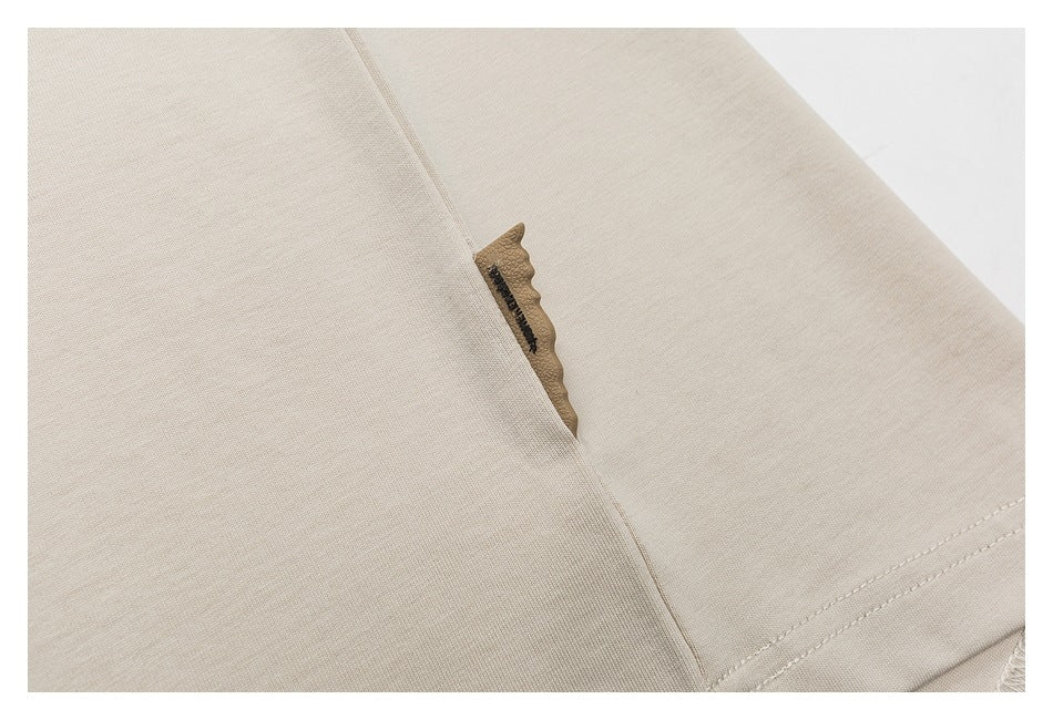 Close-up of beige shirt fabric and stitching beside a small tan decorative detail.