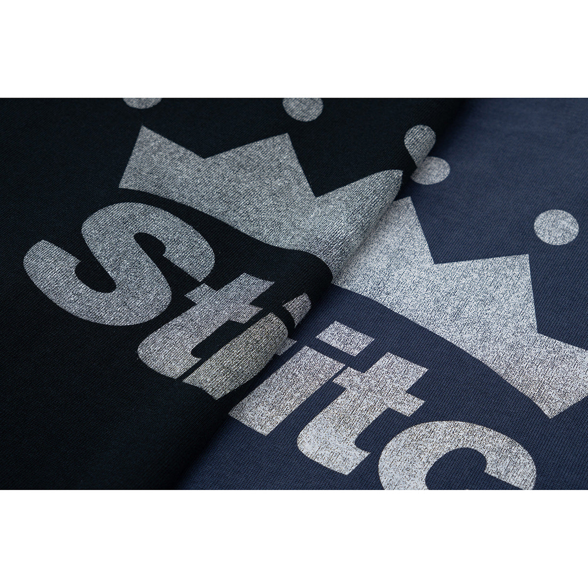 Close-up of a large silver crown and wordmark printed on dark navy T-shirt fabric.
