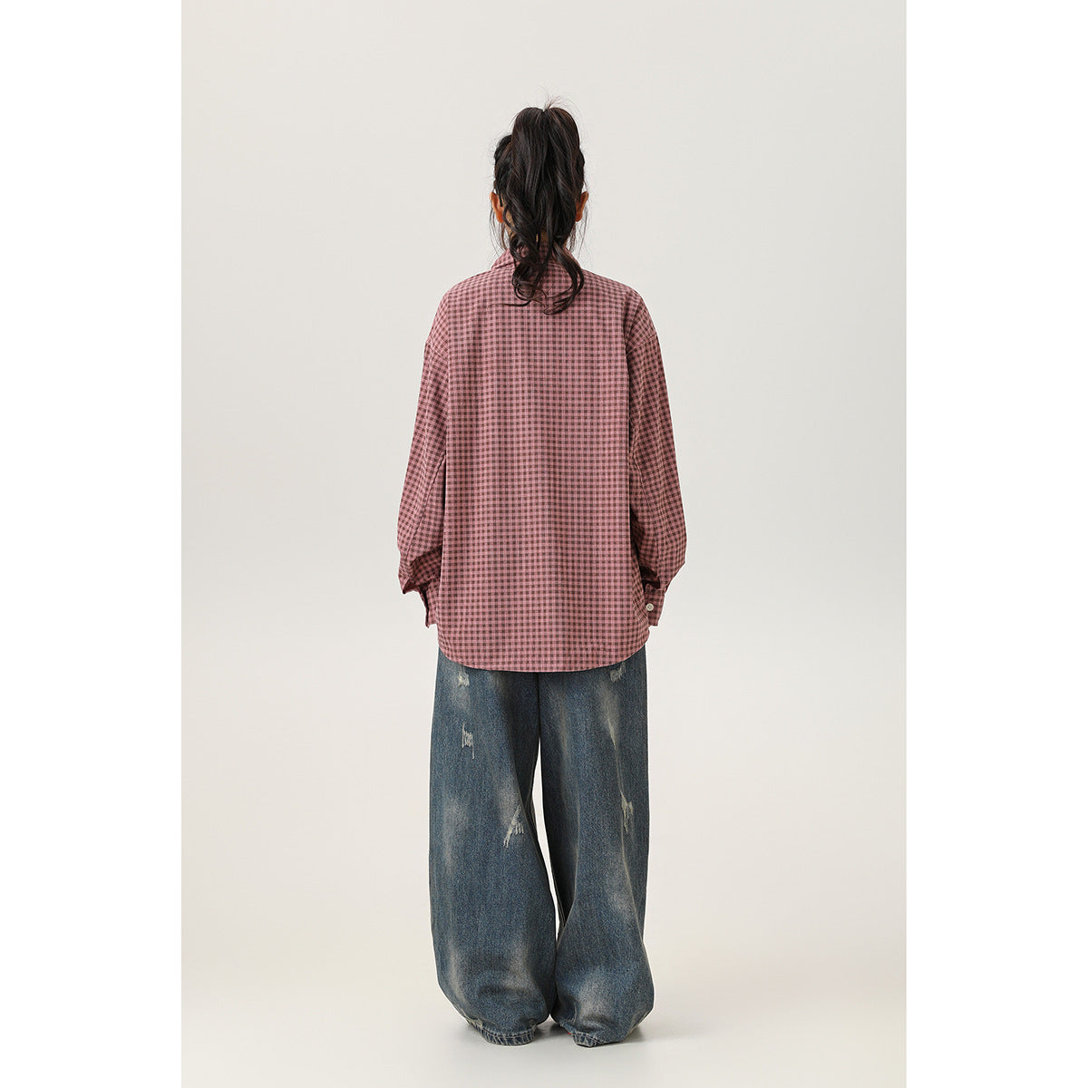 Rear view of a model wearing an oversized dusty-pink check shirt and loose distressed jeans.