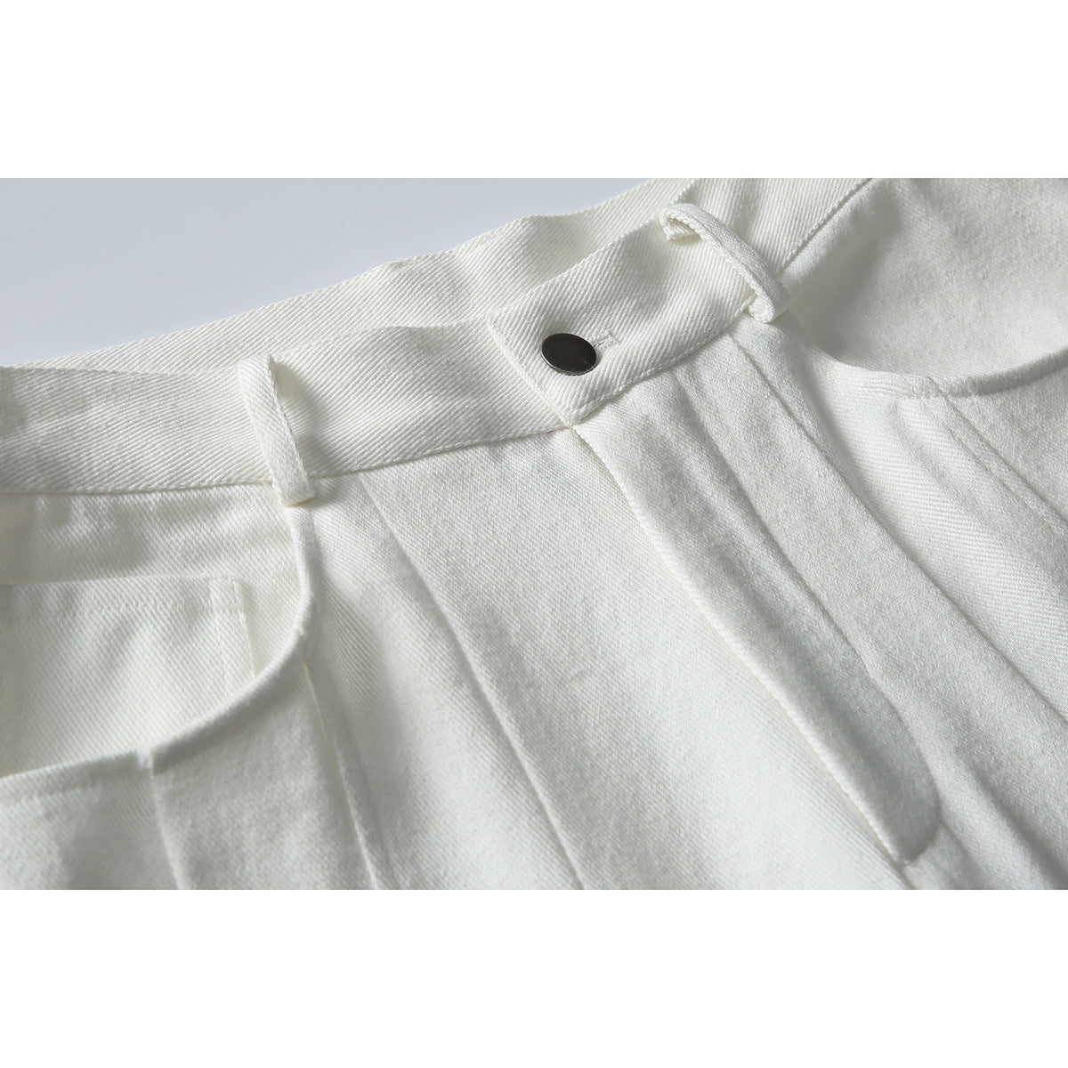 Close-up of white trousers showing the waistband, belt loop, dark button, and front pleats.