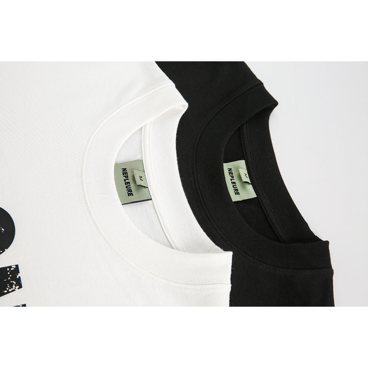 Close-up of overlapping white and black T-shirt collars with green neck labels.