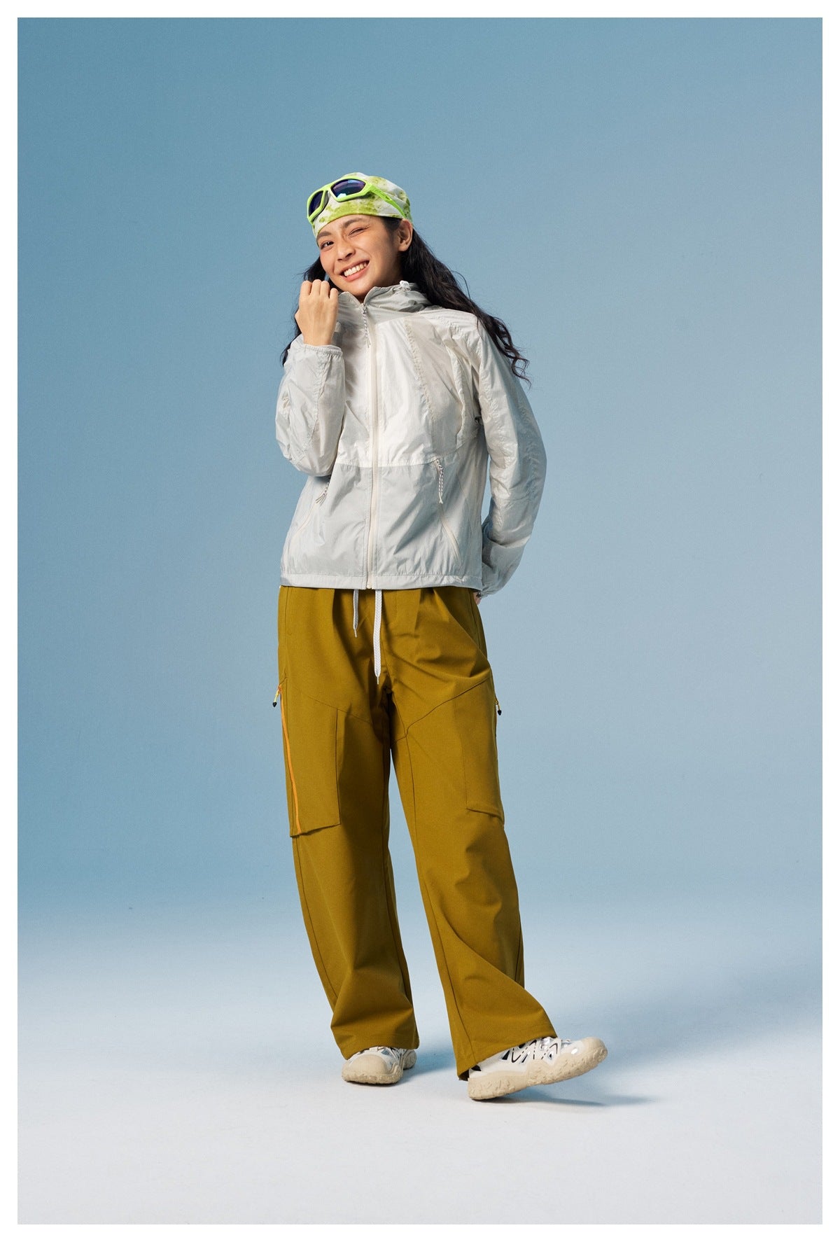 Model in the white zip-front hooded jacket with one hand raised, styled with olive wide-leg pants and sneakers