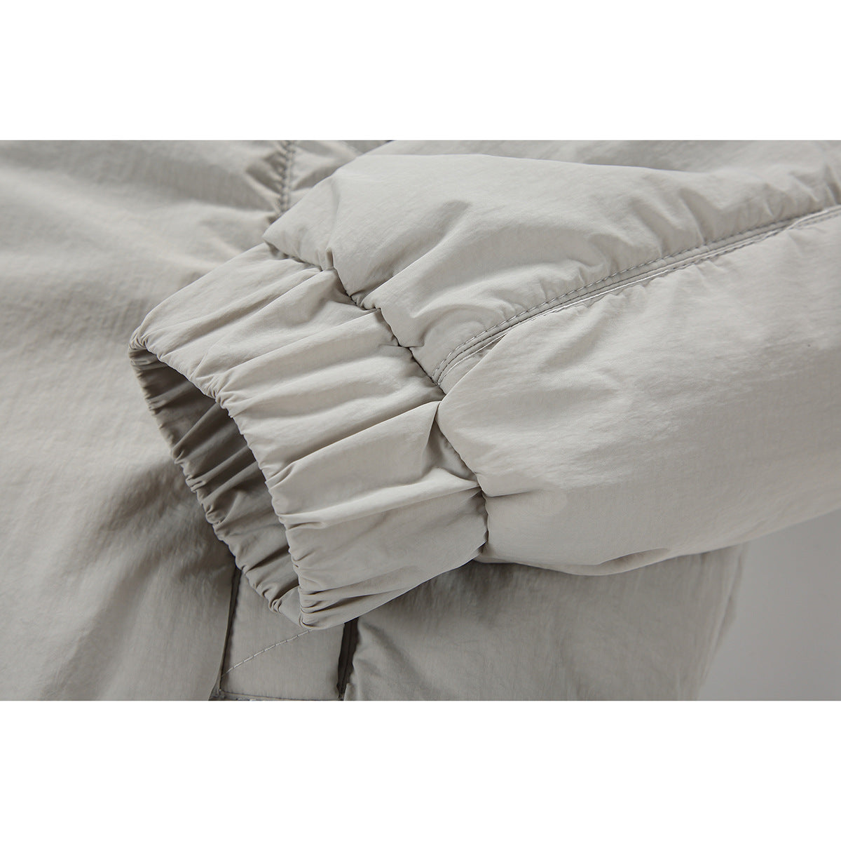 Close-up of a light gray jacket’s gathered sleeve cuff and stitched seam.