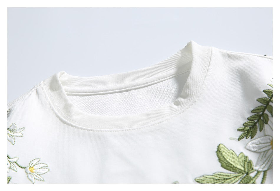 Close-up of a white T-shirt's ribbed crew neck with partial green leaf and white flower embroidery.