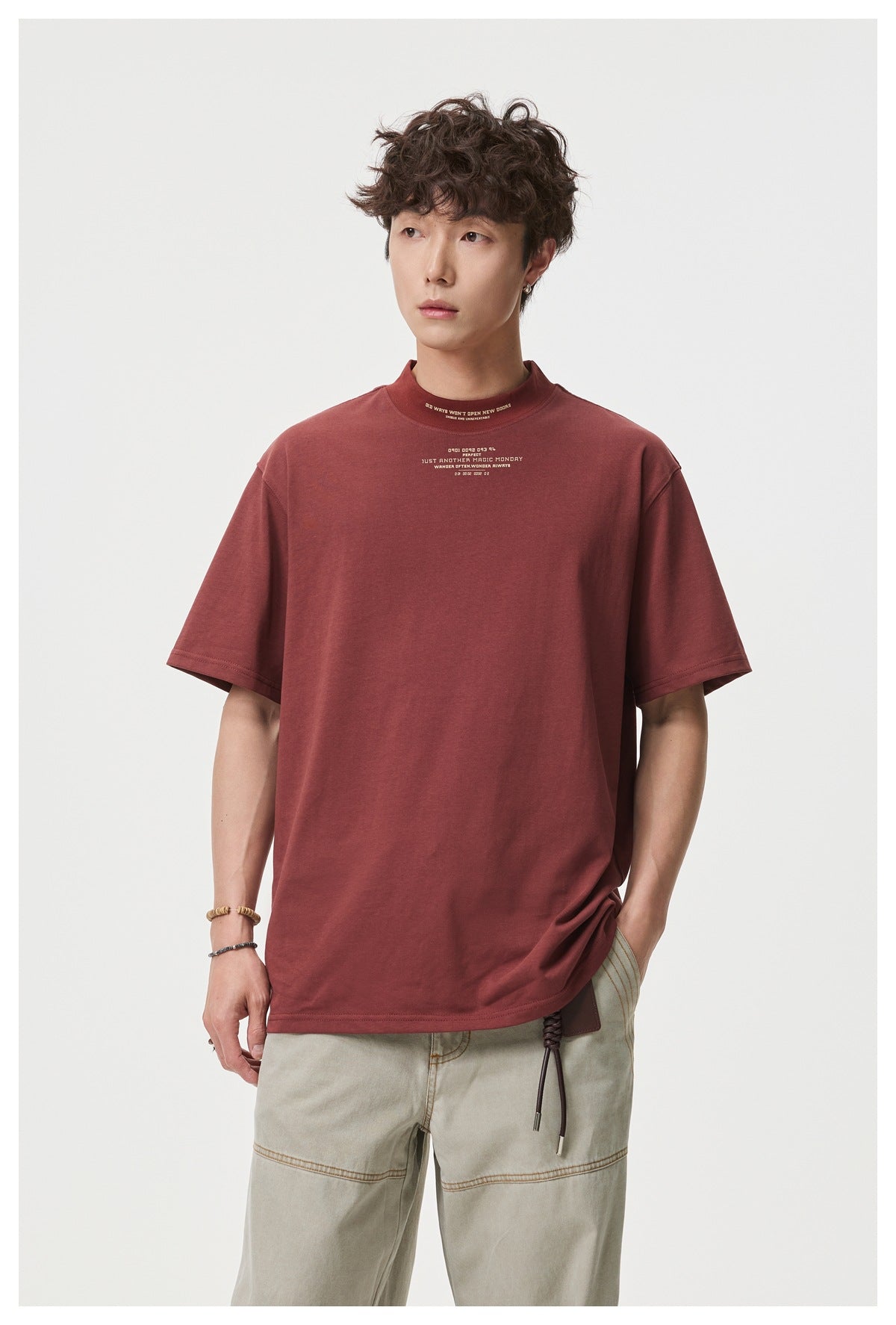 Model wearing a burgundy short-sleeve T-shirt with a high crew neck and small cream chest and collar text.