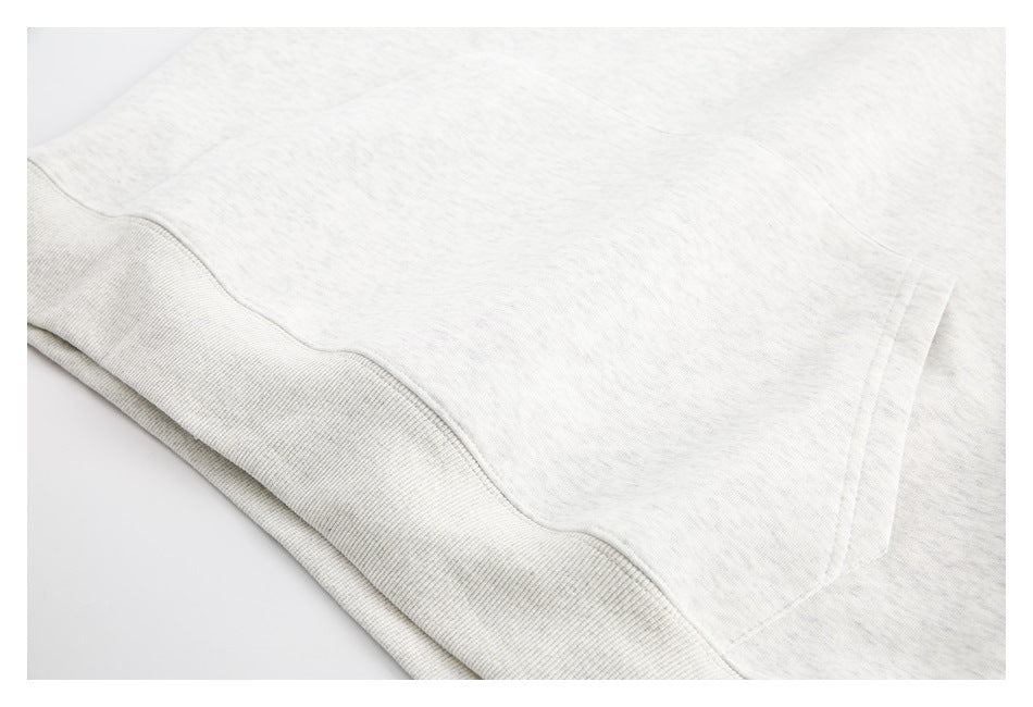 Close-up of the kangaroo pocket and ribbed hem on a light heather gray hoodie.