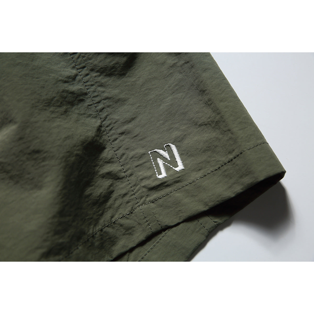 Close-up of an olive-gray shorts hem with a small white embroidered letter N.